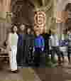 Group of smiling attendees of a B Local event standing inside a cathedral beneath arched ceilings, with a B Corp logo illuminated on the stone wall in the background.