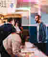 An indoor B Lab event where people network in a room with blue paneling and white ornate,  a woman writes her ideas on colourful sticky notes on a large table in the foreground.