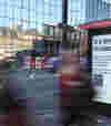 A bus shelter featuring a B Corp advertisement that reads, "It’s time to step up," with blurred pedestrians passing by.